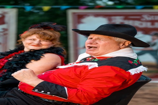 Slim and Trixie in red and black western costumes singing at the Wild West Murder Mystery.