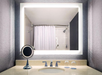 Modern bathroom with a lighted mirror, countertop sink, and a small round mirror. A shower with a white curtain is reflected in the mirror. Two glasses are placed on the counter.