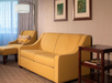 Yellow couch and patterned armchair in a living room with a floor lamp, framed art, and a wooden side table.