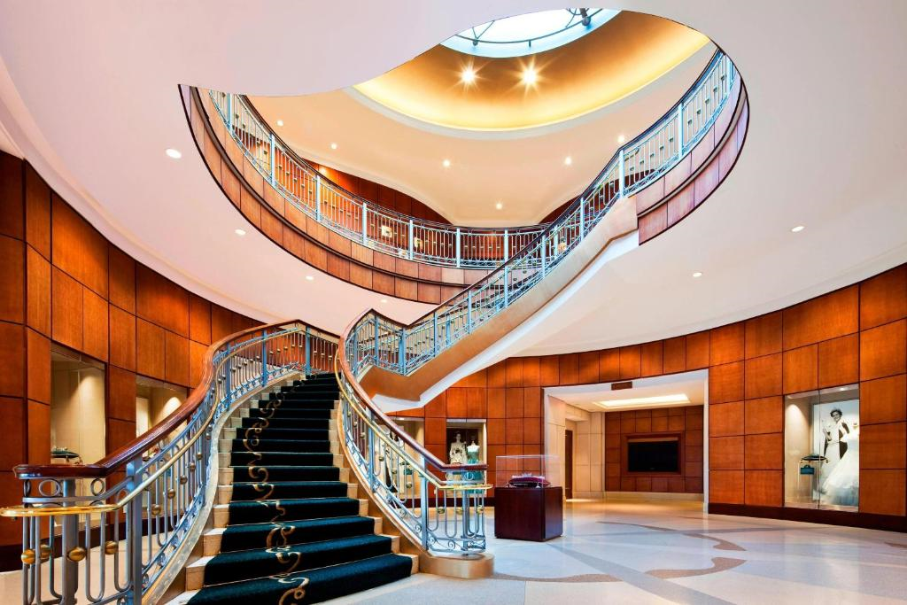 Elegant spiral staircase with wooden paneling and a skylight, surrounded by luxury displays in a spacious, well-lit atrium.