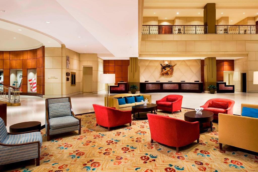 Hotel lobby with colorful seating, including red and blue armchairs, a patterned carpet, and a reception desk in the background.