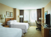 Hotel room with two double beds, a small sitting area, desk, TV, and large windows with curtains.