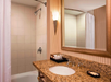 Bathroom with a granite countertop, sink, mirror, and wall-mounted light. A shower with a curtain is on the left. A soap dish and toiletries tray are placed on the counter.