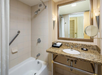 A bathroom with a shower and bathtub combo, granite countertop sink, mirror, and beige tiled walls.