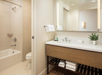 A modern bathroom with a bathtub, toilet, and a vanity. The vanity has a mirror, sink, towels, toiletries, and a small plant.