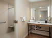 Accessible bathroom featuring a roll-in shower with grab bars, a fold-down seat, and a vanity with an illuminated mirror.