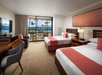 Two queen beds, seating area, work desk, flat-screen TV, and private balcony inside a guest room with beach view.
