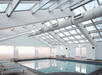 Indoor swimming pool with skylights and large ventilation ducts. Several poolside chairs are on the left side.
