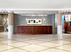 Hotel lobby with a wooden front desk, geometric tiled floor, overhead lighting, and framed artwork on the back wall.
