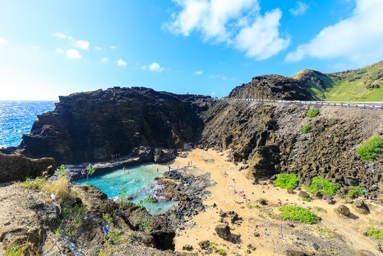 Aerial view looking over Halona Beach Cove at the Halona Blowhole Lookout with people playing in the water on sunny day.
