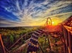 A roller coaster with a train full of riders curves along its tracks at sunset, with dramatic clouds and forested landscape in the background.
