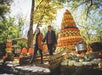 A couple walks hand in hand past a large decorative pumpkin display and assorted gourds at an outdoor autumn festival.
