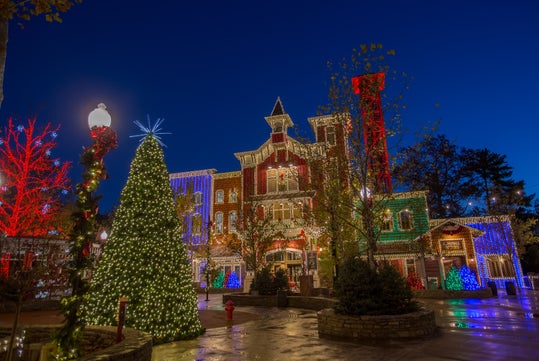 A building and large tree are adorned with colorful Christmas lights, set against a clear, deep blue evening sky.