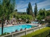 Outdoor swimming pool area with lounge chairs, umbrellas, and surrounding trees. A white fence and hedges border the pool.