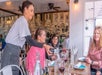 A waitress pours red wine for three women sitting at a restaurant table. The setting has a mural on the wall and a casual atmosphere.