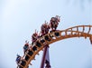 A roller coaster train full of riders travels along a curved, elevated section of track against a clear sky, with many riders raising their arms.