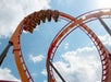 People ride an orange roller coaster as it loops upside down against a blue sky with scattered clouds.