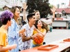 A group of people enthusiastically playing a carnival basketball game outdoors, with laughter and anticipation evident on their faces.
