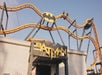 Theme park roller coaster entrance with a Batman logo and yellow track loops against a clear sky.
