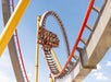 A roller coaster with riders suspended in seats moves through a vertical loop under a clear blue sky.