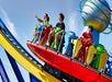 People riding a colorful amusement park ride with a globe structure on top, against a blue sky backdrop.
