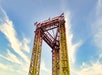 Red and yellow steel amusement park ride tower with "Fiesta Texas" sign at the top against a blue sky. Two American flags are attached to the structure.