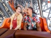 A young man and woman looking at each other and laughing while riding an orange roller coaster at Six Flags.