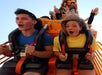 Two people on a roller coaster ride appear excited and surprised. They are secured in their seats while others in the background have their hands up.