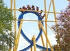 Roller coaster with blue and yellow tracks in a loop, surrounded by trees, with passengers riding through the loop on a clear day.