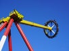 A yellow and red amusement park ride shaped like a giant pendulum swings riders against a clear blue sky.