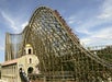 A large wooden roller coaster with a train of riders descending a steep hill, next to a building labeled "El Toro" under a partly cloudy sky.