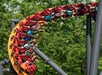 People riding a roller coaster with an orange track, surrounded by green trees.