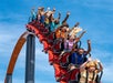 People riding a roller coaster with arms raised against a clear blue sky.