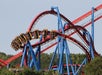 A roller coaster with multiple loops and blue support beams is pictured against a clear sky, with trees visible at the bottom.