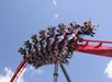 Roller coaster sharply turns upside down as riders, secured in seats, raise their hands and scream against a background of blue sky and clouds.