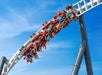 A roller coaster with riders hanging upside down while speeding through an inverted loop against a clear blue sky.