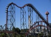 A roller coaster with a steep drop and several loops is pictured against a clear blue sky, with a tall observation tower visible in the background.