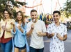 A group of four people walking and enjoying ice cream together at Six Flags New England with a roller coaster in the background.