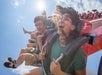 Two people screaming in excitement aboard the Harley Quinn Spinsanity pendulum ride as they swing out mid air.