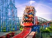 A red roller coaster with a "Superman" logo ascends a steep track with riders holding their arms up. Blue support beams and a colorful track are visible against a bright blue sky.