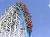 People riding a roller coaster with raised arms, traveling down a steep blue and white track against a clear blue sky.