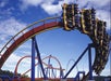 Roller coaster with passengers riding through a loop against a clear blue sky, supported by colorful metal structures.