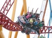 A group of people ride a fast roller coaster with red tracks and yellow supports, some with hands up and expressions of excitement.