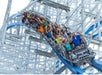 A roller coaster car full of people descends a steep track, with many riders raising their hands and expressing excitement. The structure is blue and white steel.