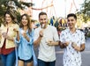 Four people walking outside, eating ice cream and smiling, with amusement park rides in the background.