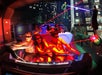 People wearing 3D glasses in an interactive ride with superhero and city graphics, aiming laser guns at targets.