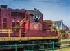A train with a red engine car with the number 65 and the conductor on the train waving.