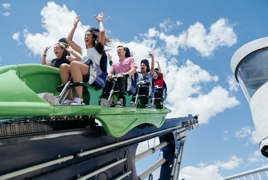 People screaming with their arms up riding X-Scream at The STRAT on a sunny day in Las Vegas, Nevada.