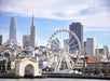 Skyline featuring a Ferris wheel in front of modern and classic buildings under a clear blue sky.