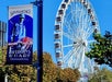 A Ferris wheel stands beside a "San Francisco Fisherman's Wharf" banner near trees, against a clear blue sky.